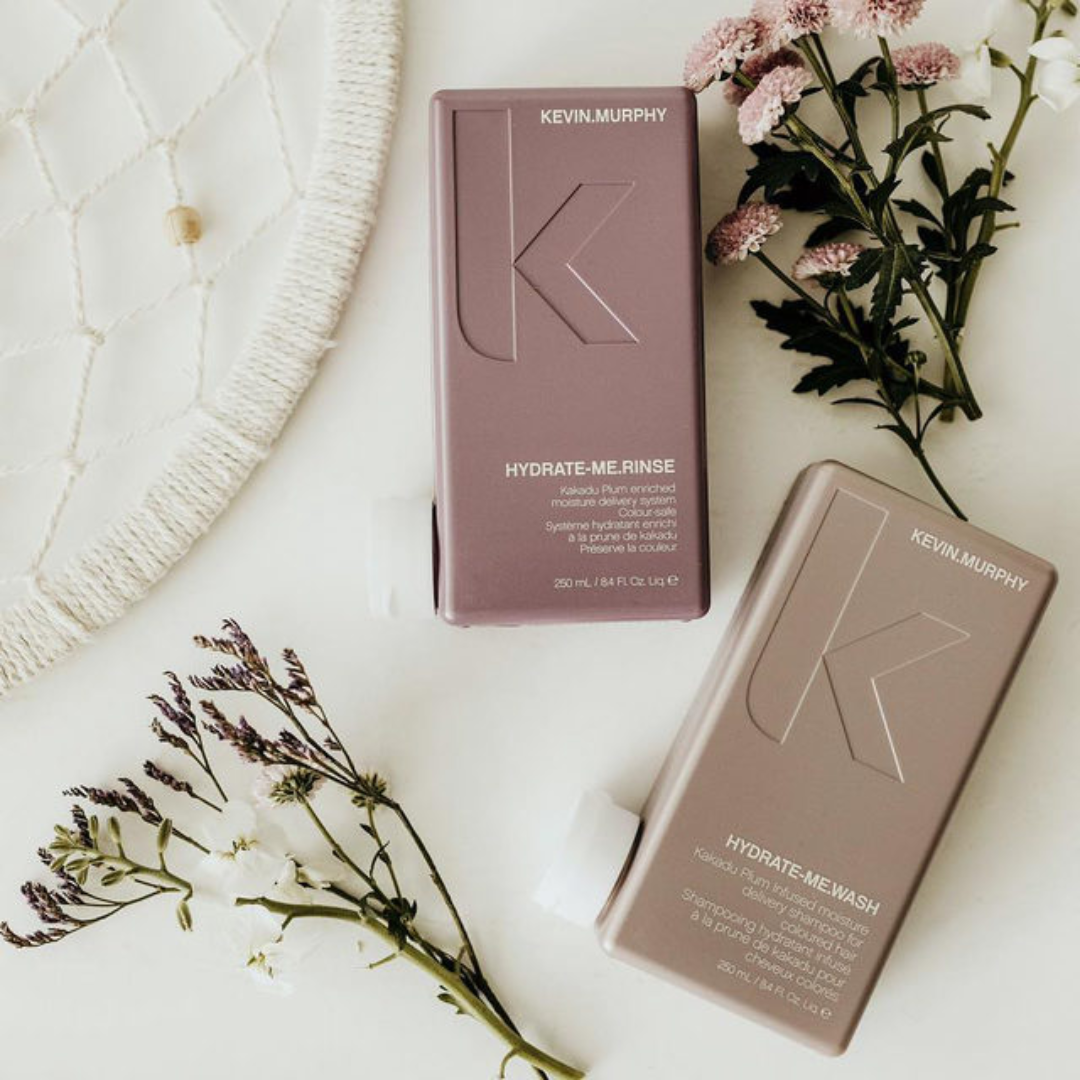 Kevin Murphy Hydrate-Me Wash and Rinse bottles displayed on a white surface with decorative flowers.