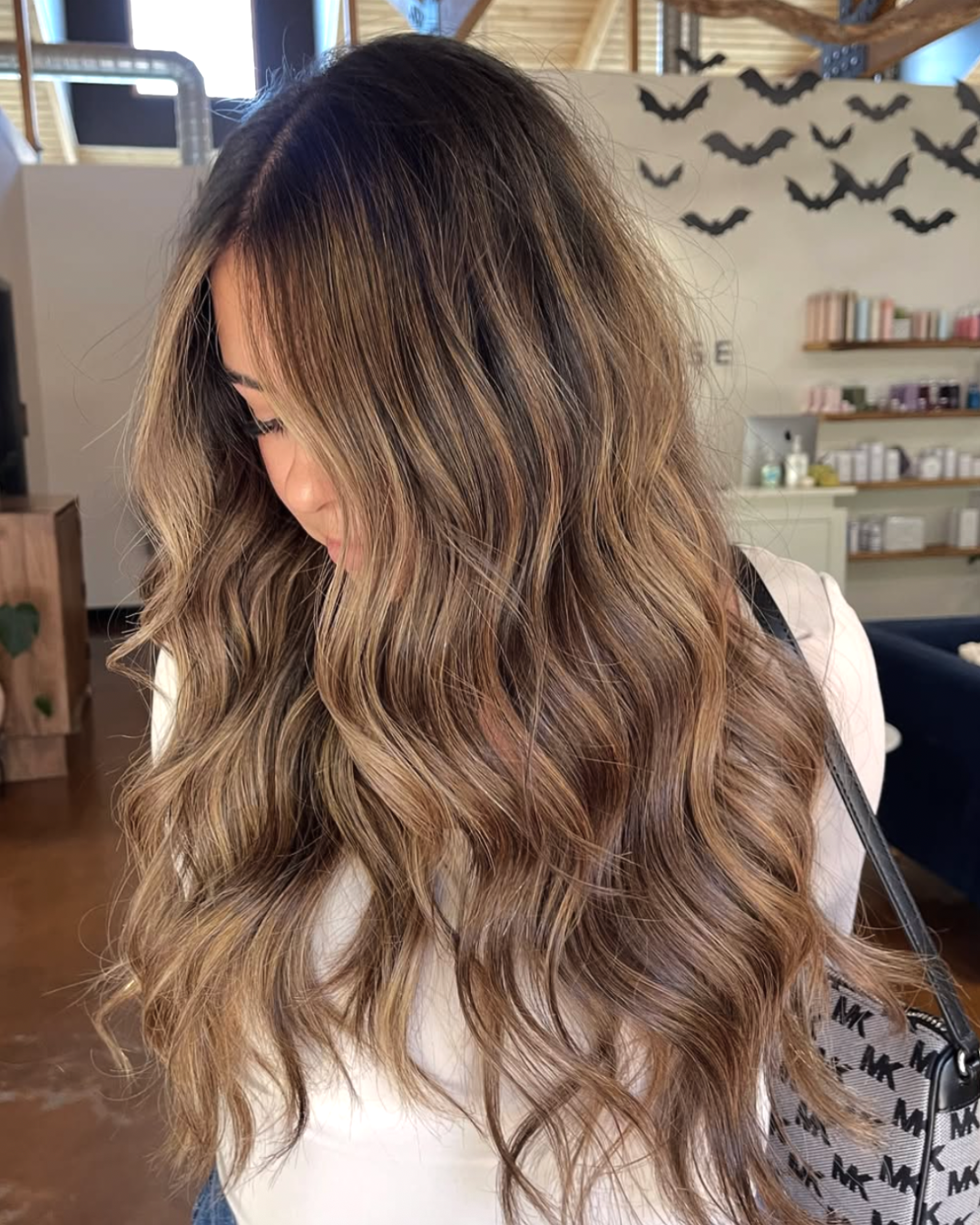 Woman with long wavy balayage hair featuring blended brunette roots and soft caramel blonde highlights.