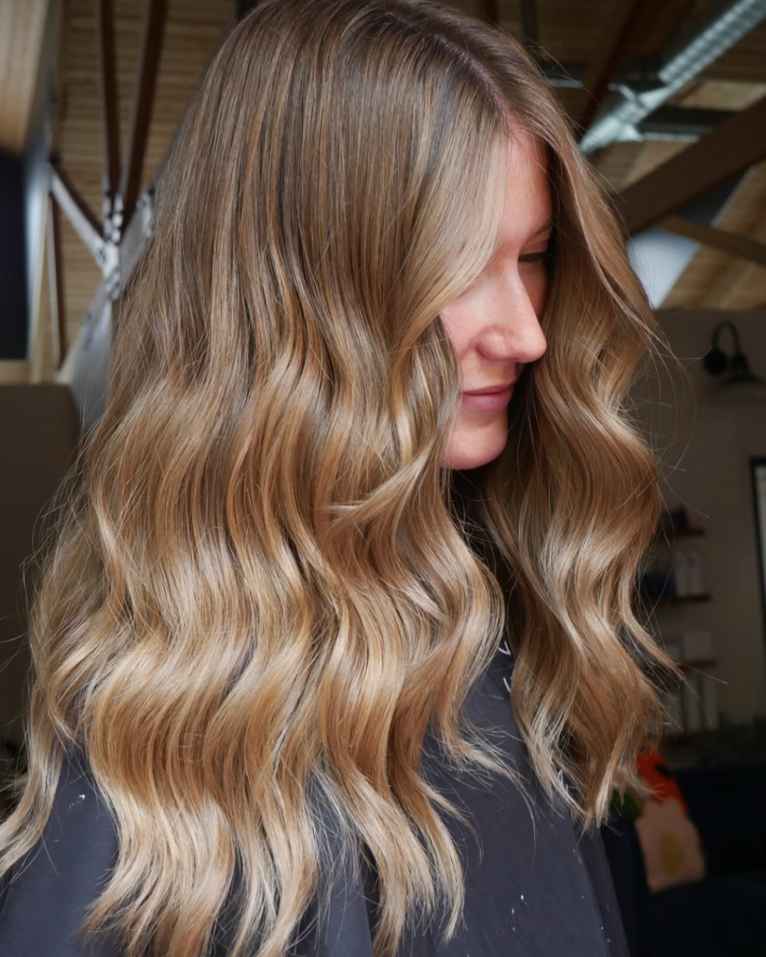 Woman with long wavy blonde balayage hair featuring blended brunette roots and warm blonde highlights.