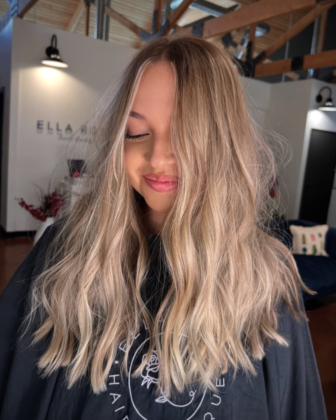 Woman with long layered beige blonde hair styled in soft waves after a blonding service and haircut.