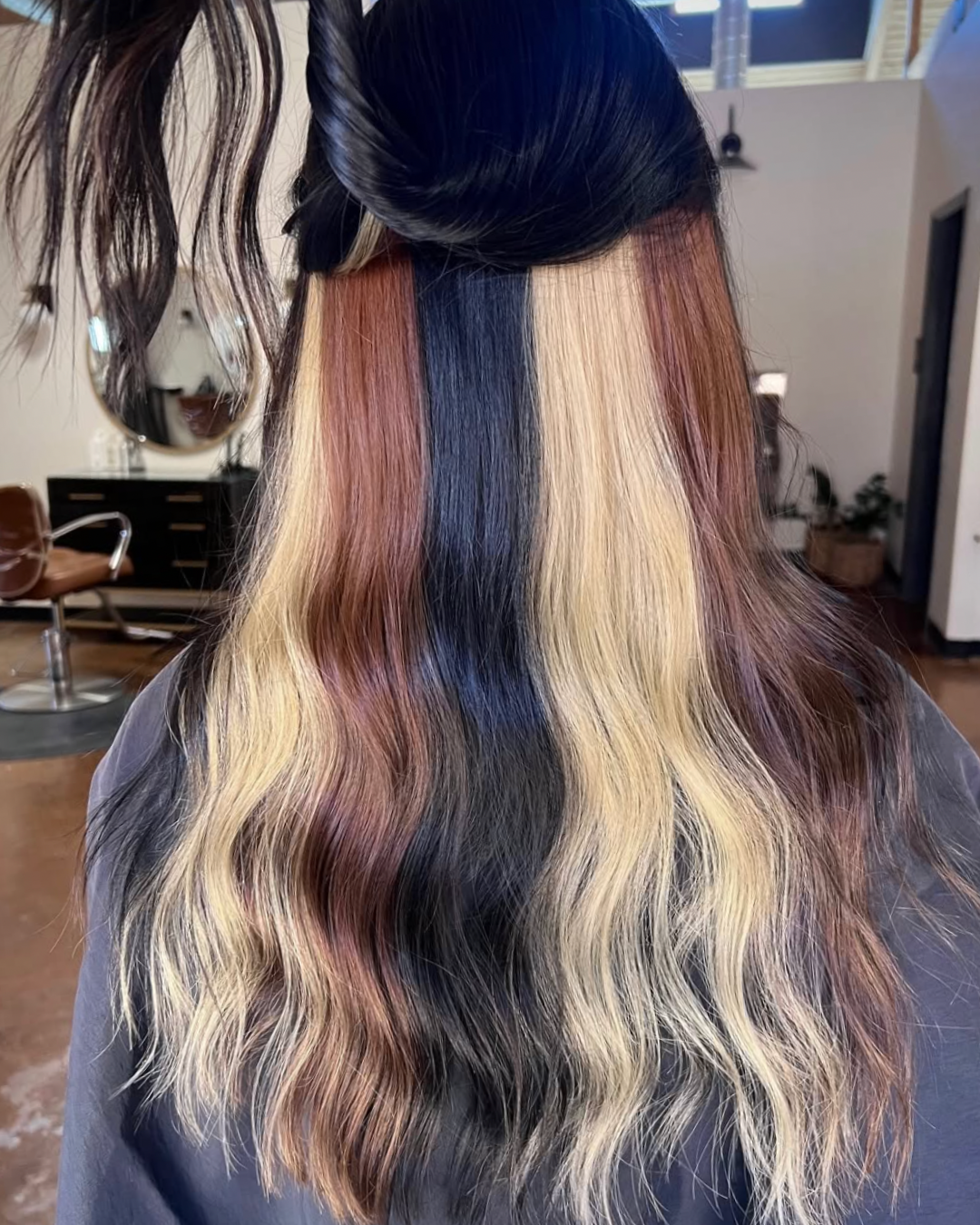 Back view of a woman with calico hair color featuring large sections of blonde, black, and brunette hair blended in bold panels, creating a high-contrast, multi-tonal look.