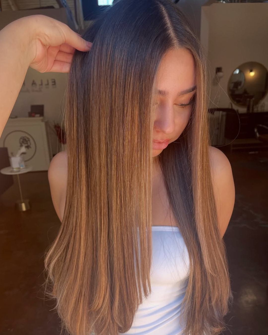 Woman with long and straight hair in a caramel brunette color with a deeper, dark brunette root