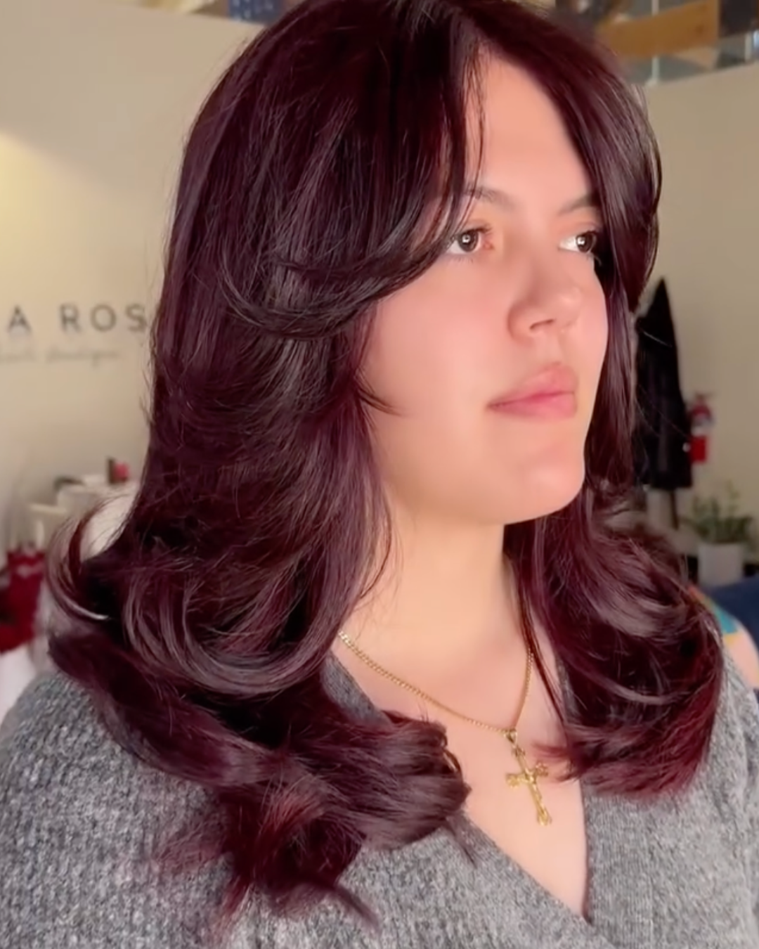 Woman featuring medium length cherry cola colored hair with curtain bangs and short + long layers