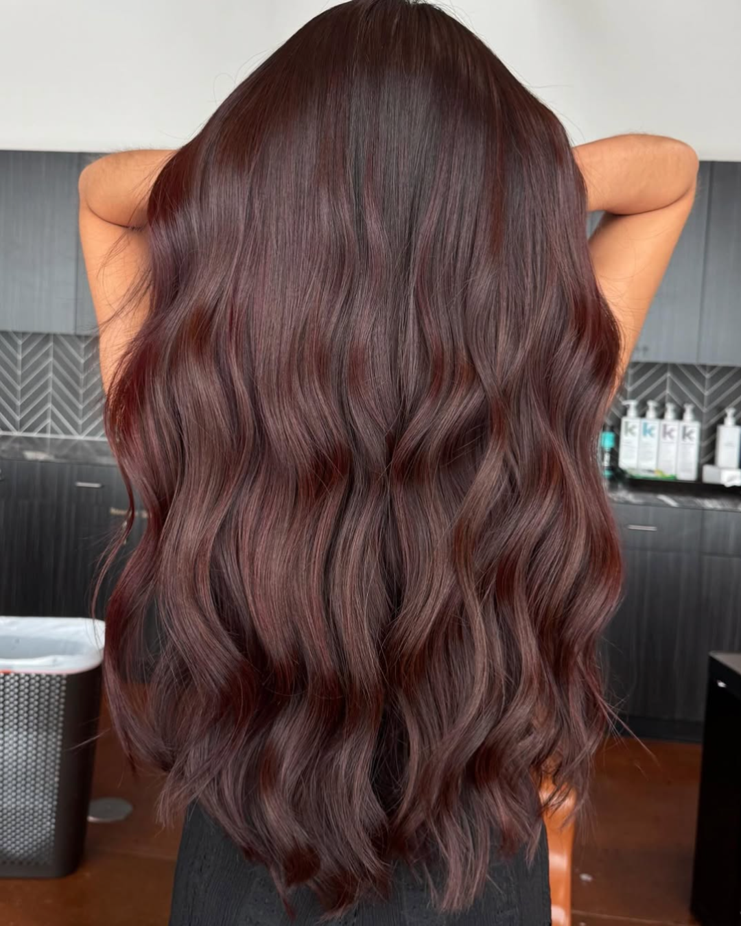 Woman with long, waist length full hair in a deep, dark cherry cola color