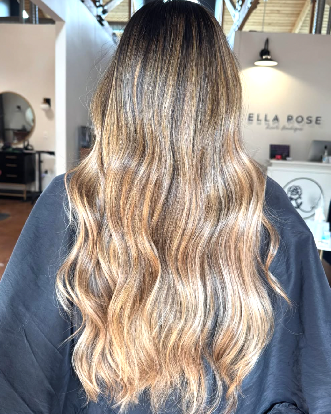 Back view of a woman with darker brown roots and lighter blond ends with dimension throughout