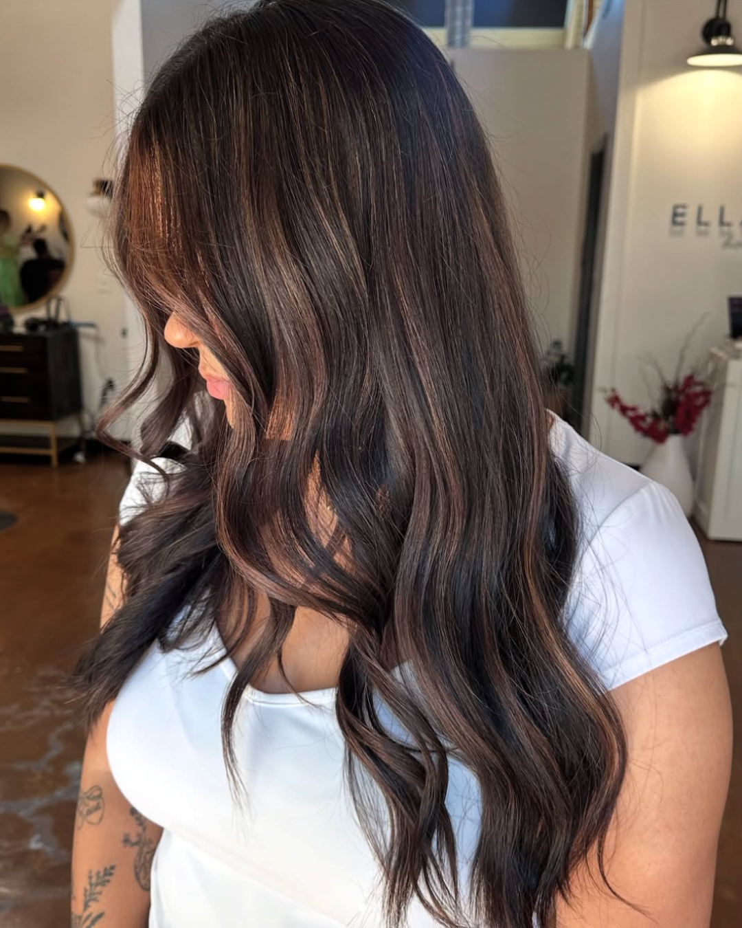 Side view of a woman with long, dark brunette hair with a balayage featuring soft, caramel dimension