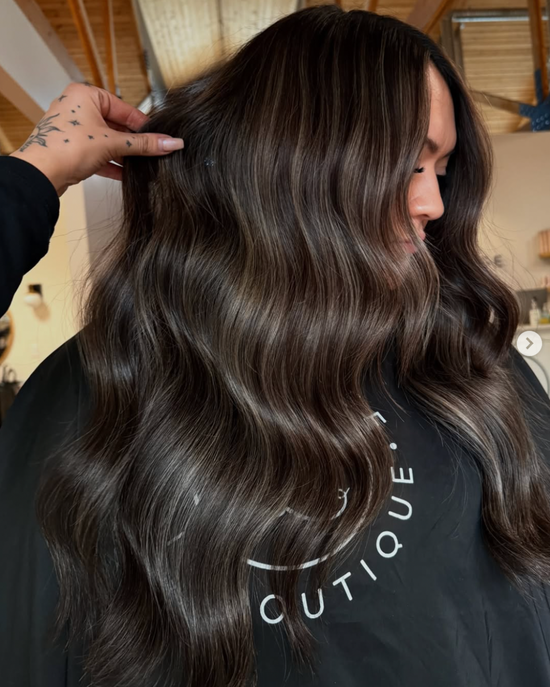 Side view of a woman with long, wavy hair featuring a dimensional mocha brunette color