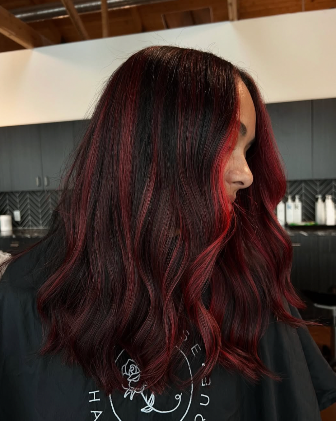 Side view of a woman with a dimensional red balayage featuring deep dark brunette hair and vivid red highlights and face framing