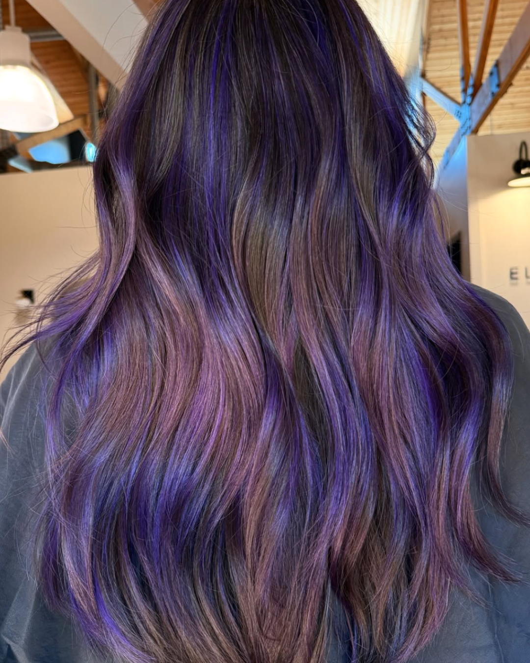 Back view of a woman with long dark brown hair, filled with electric violet highlights