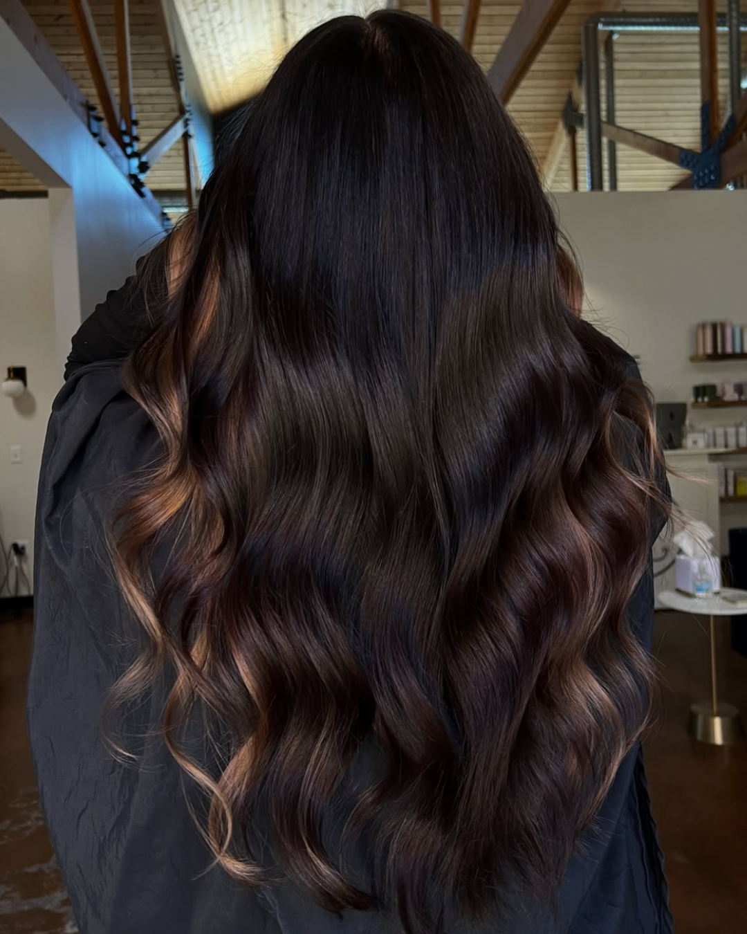 Back view of a woman with long, dark chocolate hair and caramel face framing pieces