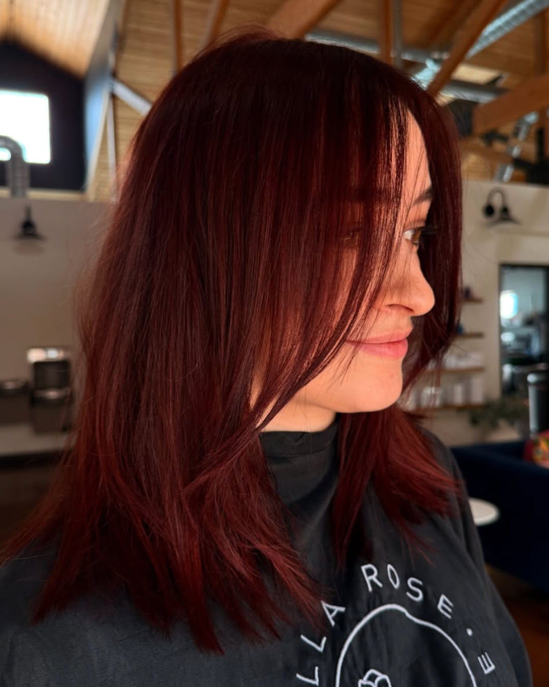 Side view of a woman with shoulder length hair featuring a rich, foxy red color and face framing layers