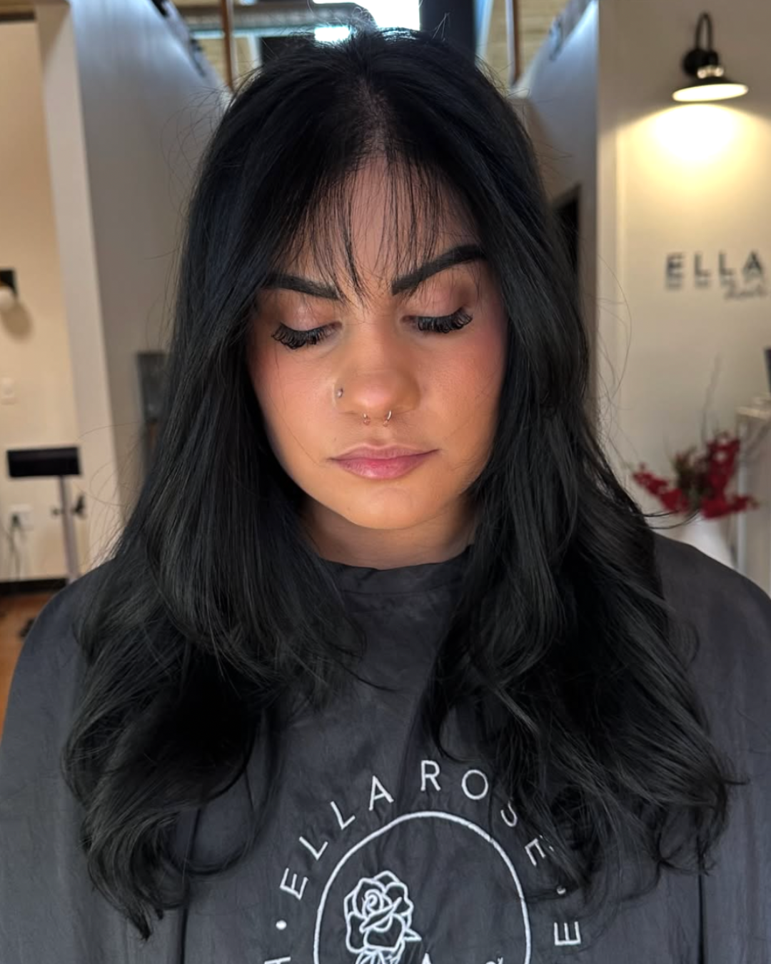 Woman with jet black hair featuring a check length haircut and wispy bangs with more fullness on the sides