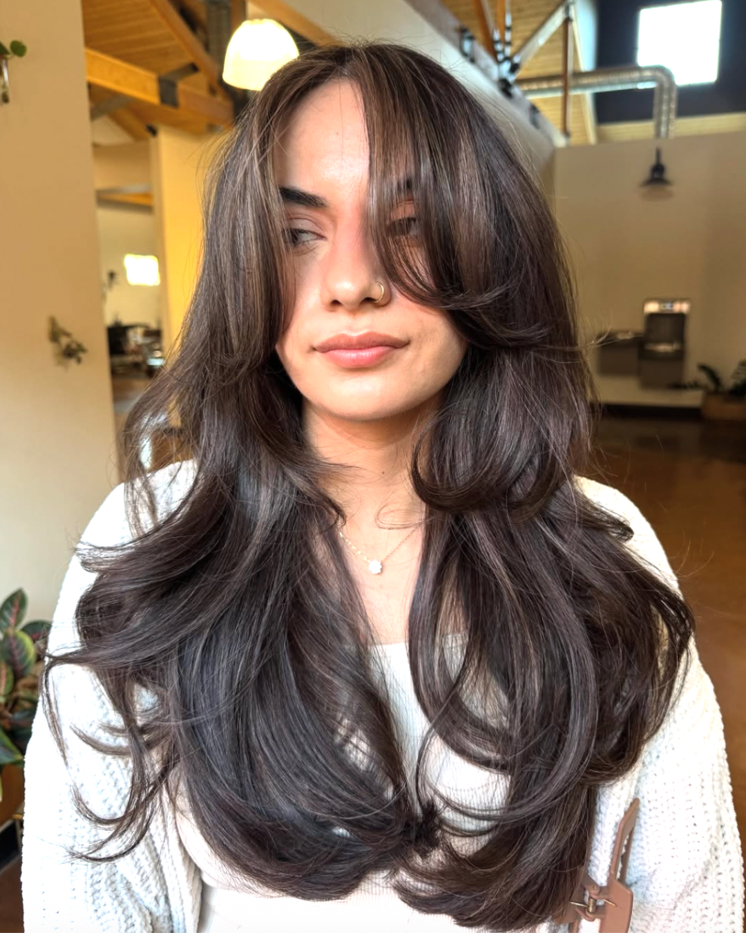 Woman with long, dark brunette hair and a mix of short and long layers with curtain bangs