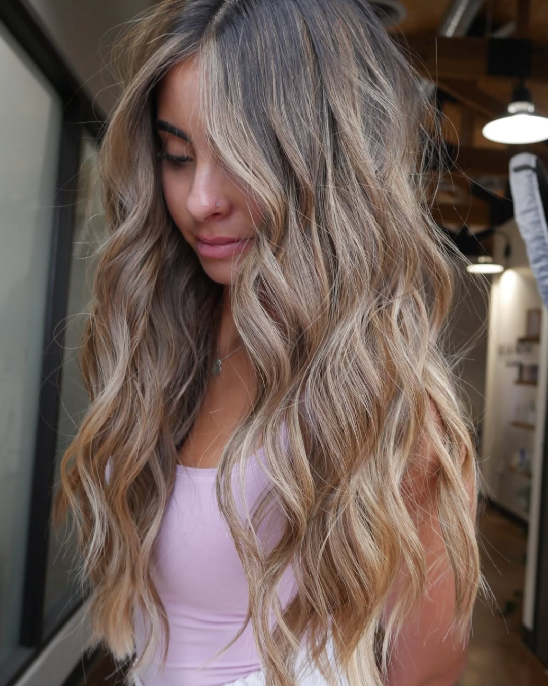 Woman with long lived-in blonde hair featuring soft beige and honey blonde tones with natural root depth and loose waves.