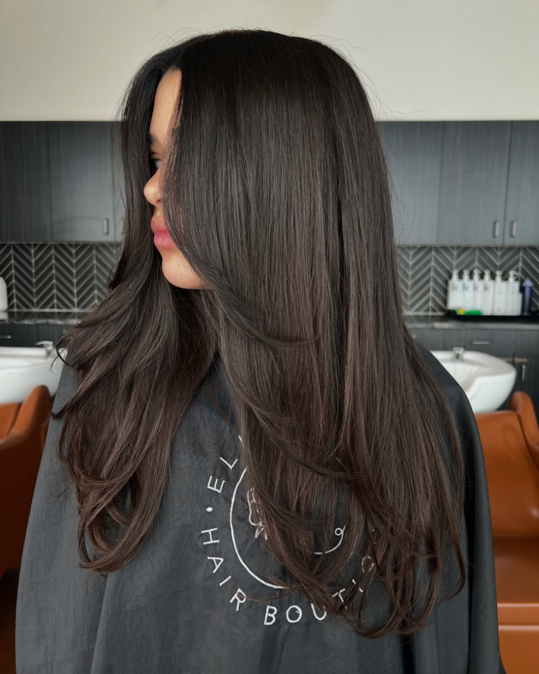 Side view of a woman with chocolate brown hair with long layers and face framing