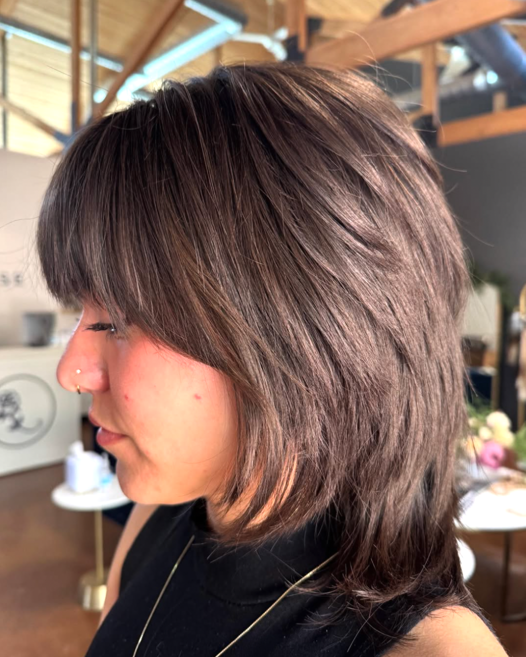 Woman with a modern mullet haircut featuring medium-length brunette hair with shaggy layers, face-framing bangs, and longer layered length in the back