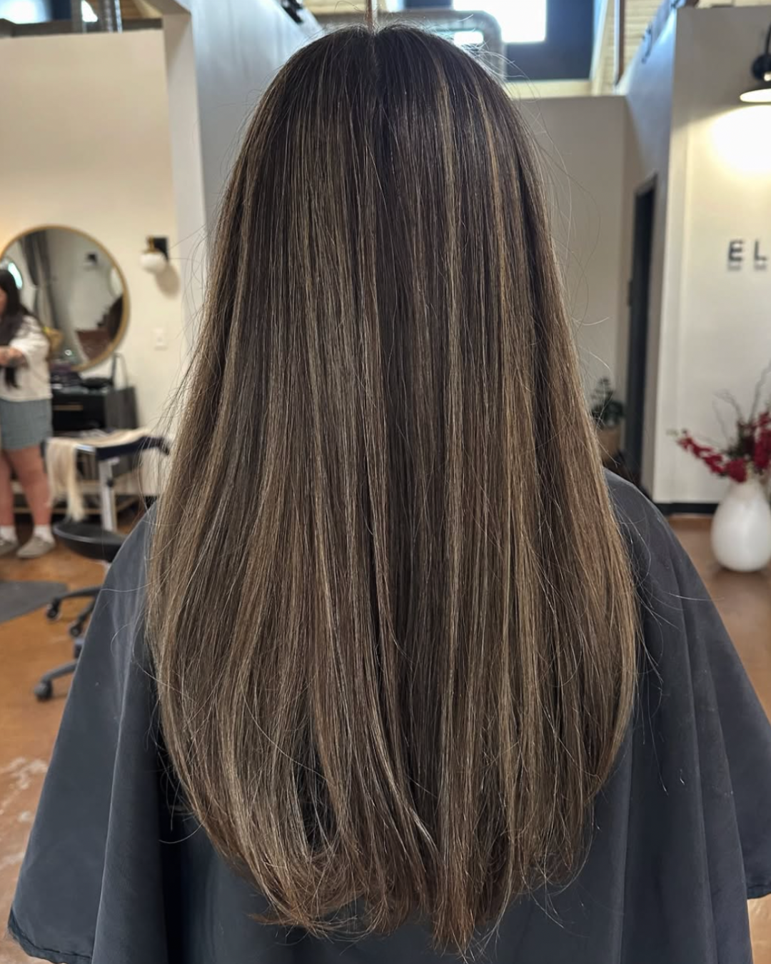 Back view of a woman with long hair featuring a soft, dimensional mushroom brunette color