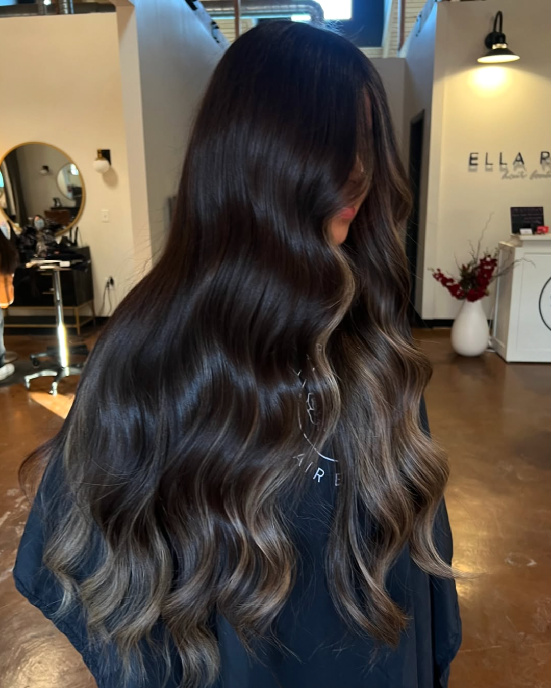 Side view of a woman with very long dark brunette hair and lighter ends and face framing pieces for an elevated balayage