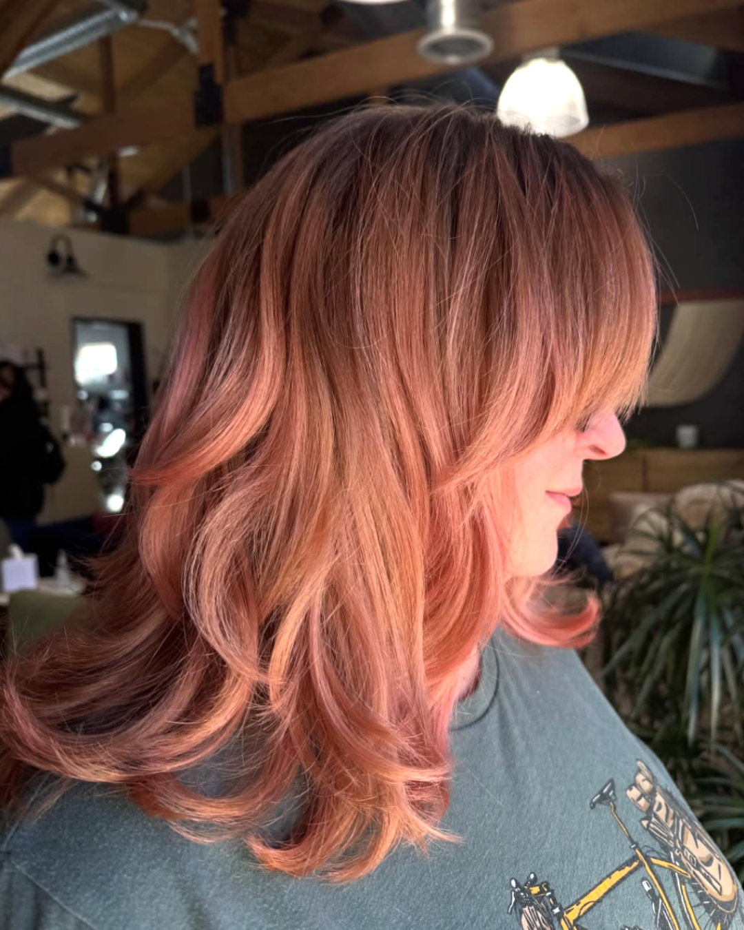 Side view of a woman with curtain bangs and voluminous layers in a rose gold color