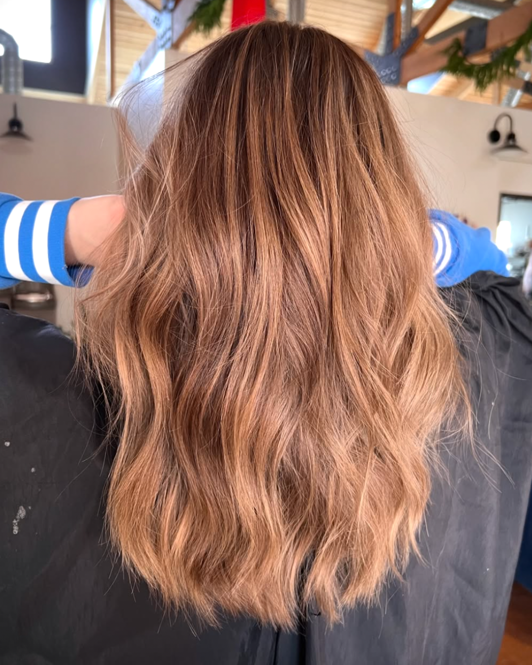 Back view of a woman with light, brunette hair with lighter brunette pieces throughout for a teddy bear look