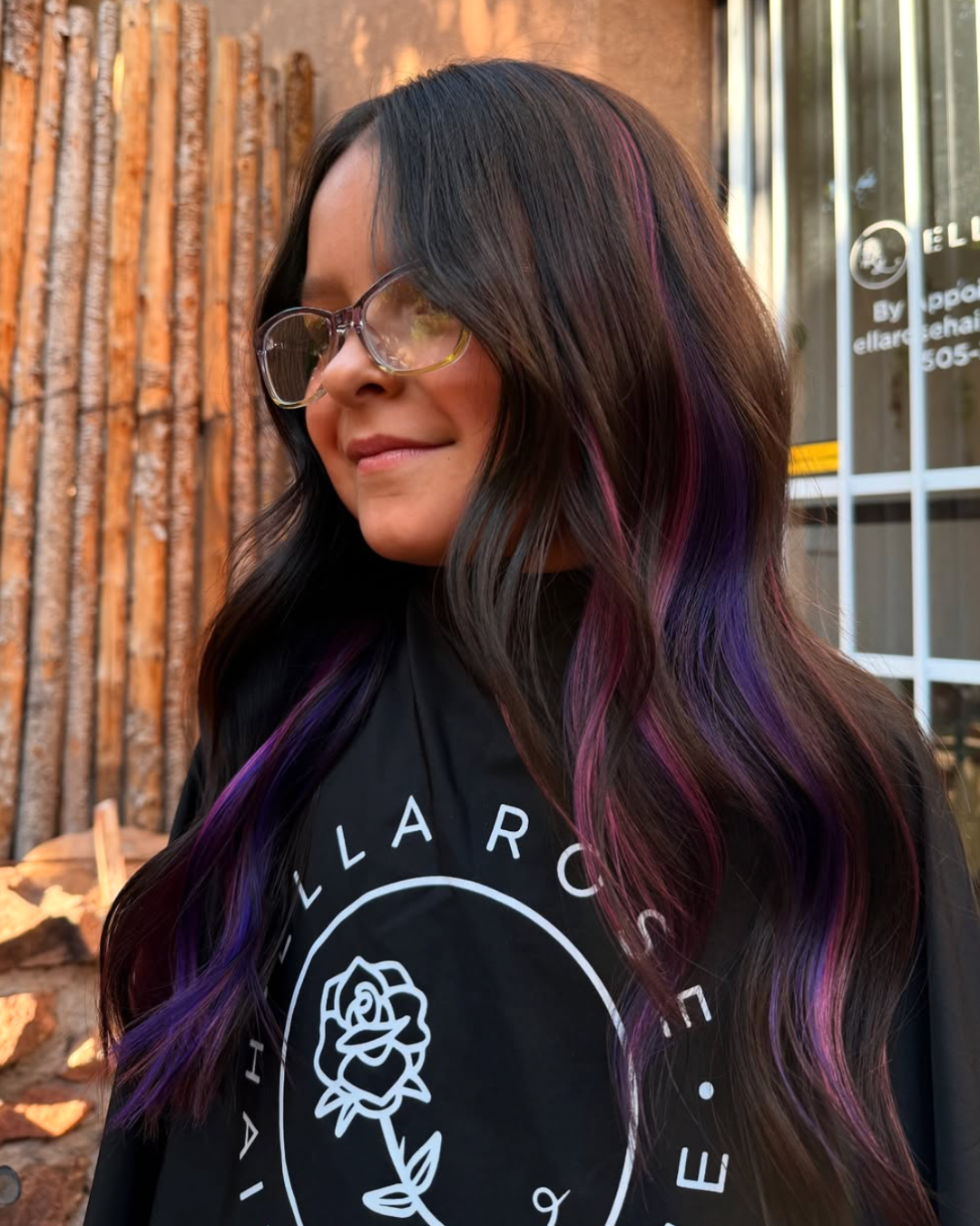 Woman with long, dark brunette hair featuring a unicorn style with pink and purple highlights throughout