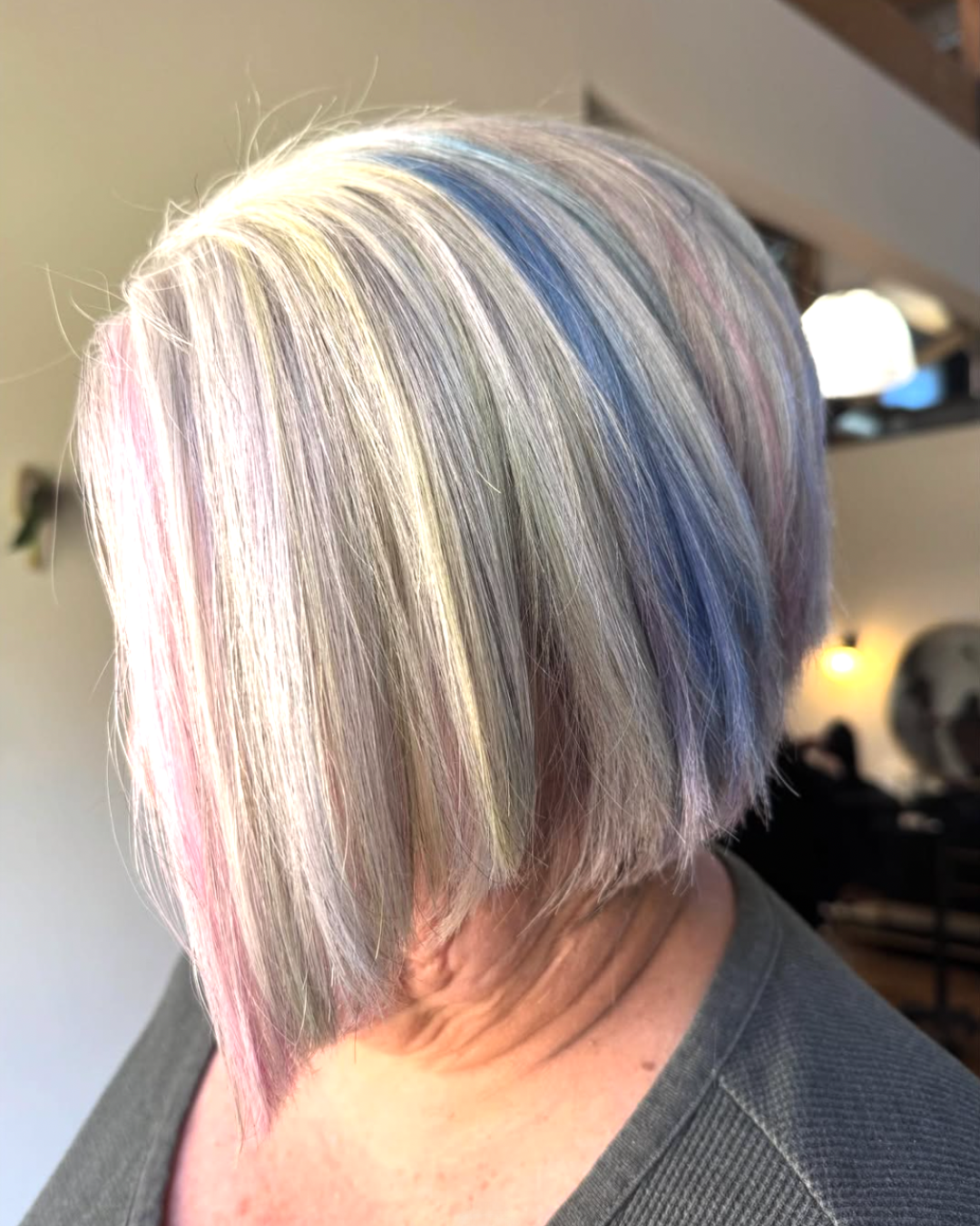 Side view of a woman with a short bob featuring icy blonde hair with pastel unicorn colors including pink, blue, and purple.